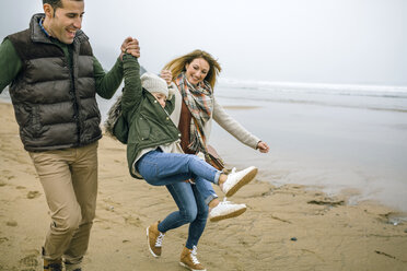 Happy parents lifting up daughter on the beach in winter - DAPF00571