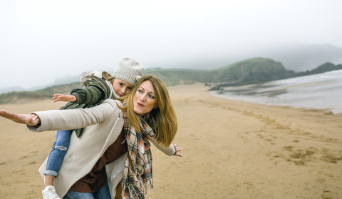 Glückliche Frau und Tochter tun so, als würden sie im Winter am Strand fliegen, lizenzfreies Stockfoto