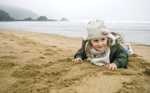 Glückliches Mädchen, das am Strand im Winter im Sand liegt - DAPF00574