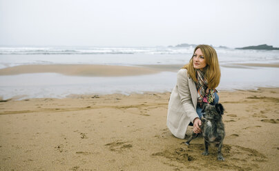 Frau streichelt Hund am Strand im Winter - DAPF00576