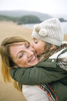 Girl kissing happy mother on the beach in winter - DAPF00580