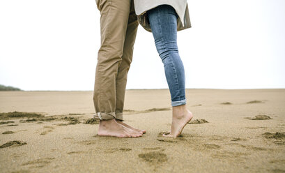 Low section of couple standing barefoot on the beach - DAPF00584