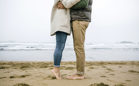 Tiefschnitt eines barfuß am Strand stehenden Paares, lizenzfreies Stockfoto