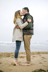 Paar steht barfuß am Strand und küsst sich - DAPF00586