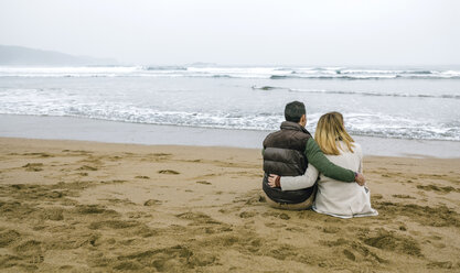 Verliebtes Paar, das im Winter am Strand sitzt - DAPF00590