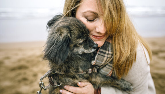 Frau, die ihren Hund im Winter am Strand umarmt - DAPF00591