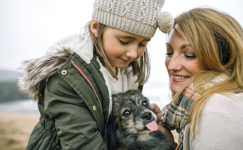 Mother and daughter stroking their dog on the beach in winter stock photo