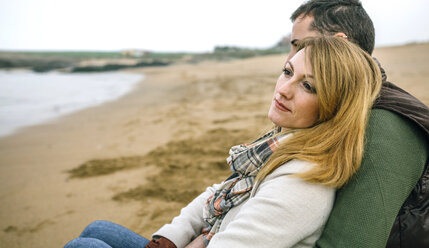 Verliebtes Paar, das im Winter am Strand sitzt - DAPF00594