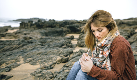 Woman with notebook sitting on rocks on the beach in winter stock photo