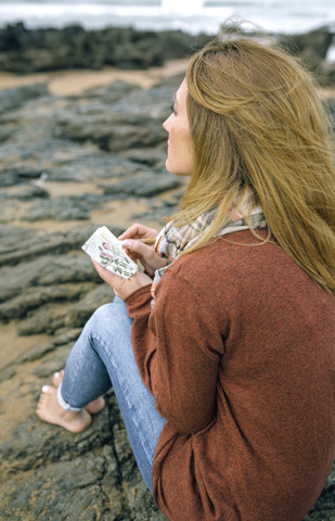 Woman with notebook sitting on rocks on the beach in winter stock photo