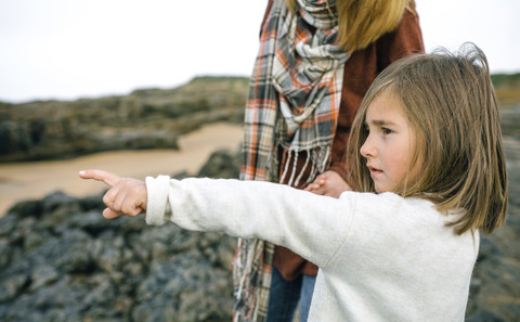 Mädchen mit Mutter zeigt mit dem Finger auf den Strand im Winter, lizenzfreies Stockfoto