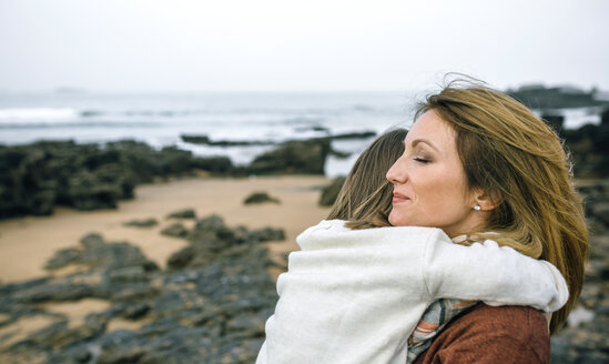 Mother holding daughter on the beach in winter - DAPF00604