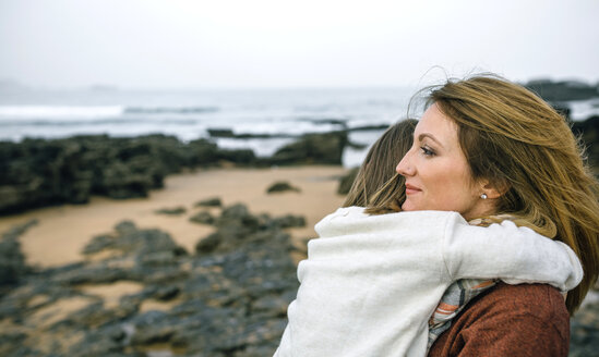 Mother holding daughter on the beach in winter - DAPF00605