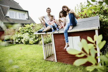 Happy family sitting on roof of their garden shed - JATF00962