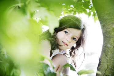 Girl crouching behind tree, looking at camera - JATF00968