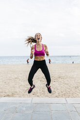 Junge sportliche Frau, die lachend über den Strand springt - GIOF01732