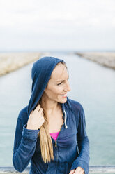 Frau mit Kapuzenjacke am Strand stehend - GIOF01750