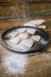 Sprinkling heart-shaped shortbreads with icing sugar on baking pan - GIOF01800