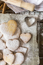 Heart-shaped shortbreads sprinkled with icing sugar and cookie cutter on parchment paper - GIOF01802