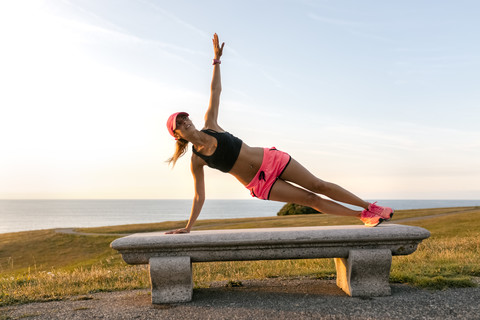 Junge Frau beim Krafttraining auf einer Bank am Meer, lizenzfreies Stockfoto