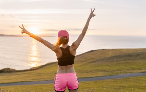 Junge Frau blickt nach dem Training mit ausgestreckten Armen auf das Meer, lizenzfreies Stockfoto