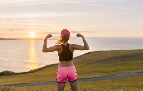 Junge Frau blickt nach dem Training auf das Meer und lässt die Muskeln spielen, lizenzfreies Stockfoto