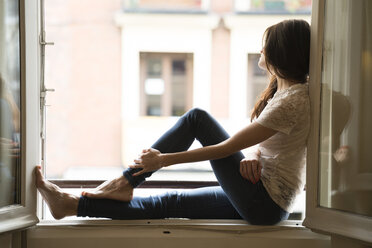 Woman sitting on window sill looking through open window - KKAF00375