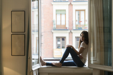 Woman sitting on window sill at open window - KKAF00377