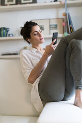 Woman on couch listening music with earphones and smartphone - KKAF00399