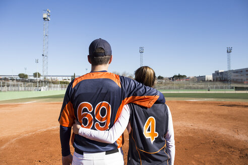 Rückansicht eines männlichen und eines weiblichen Baseballspielers, die sich auf einem Baseballfeld umarmen - ABZF01895