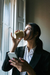 Junge Busfahrerin am Fenster, die Kaffee trinkt und ein Handy in der Hand hält - VABF01098