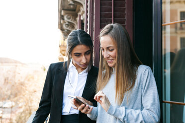 Zwei junge Frauen auf dem Balkon schauen auf ihr Handy - VABF01100