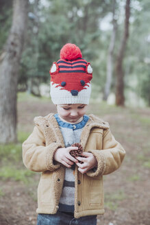 Junge mit Wollmütze hält Tannenzapfen im Wald - RTBF00627