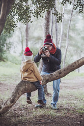 Father taking a picture of his son sitting on tree trunk in forest - RTBF00634