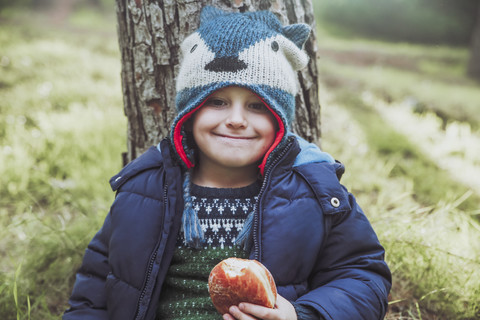 Porträt eines grinsenden Jungen, der im Wald einen Berliner isst, lizenzfreies Stockfoto