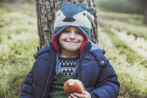 Porträt eines grinsenden Jungen, der im Wald einen Berliner isst - RTBF00644