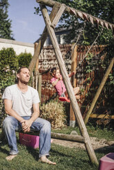 Exhausted father in garden with daughter on swing - JOSF00483