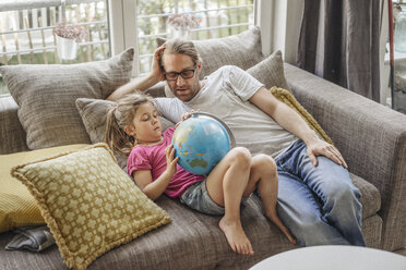 Father and daughter lying with globe on sofa - JOSF00484