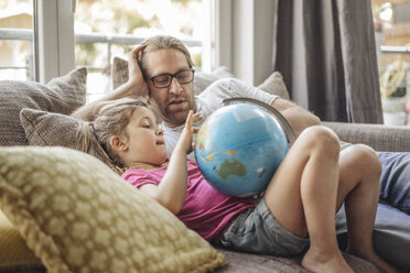 Father and daughter lying with globe on sofa - JOSF00485