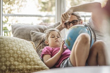 Father and daughter lying with globe on sofa - JOSF00486