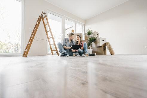 Couple sitting on floor of their new home among moving boxes - JOSF00504