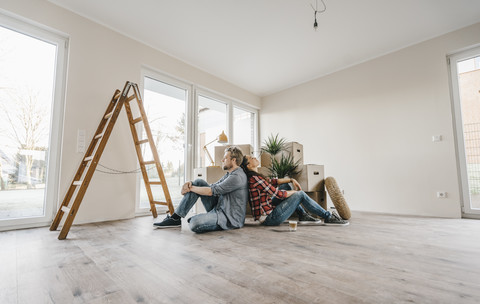 Ein Ehepaar sitzt auf dem Boden seines neuen Hauses zwischen Umzugskartons, lizenzfreies Stockfoto