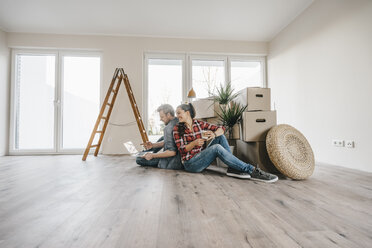 Couple sitting on floor of their new home among moving boxes - JOSF00509