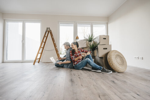 Ein Ehepaar sitzt auf dem Boden seines neuen Hauses zwischen Umzugskartons - JOSF00509