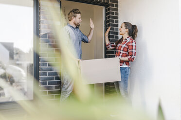 Couple carrying moving boxes into their new home, giving high five - JOSF00532