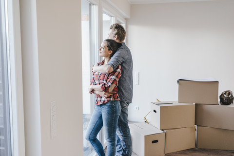 Ein glückliches Paar steht am Fenster seines neuen Hauses, lizenzfreies Stockfoto