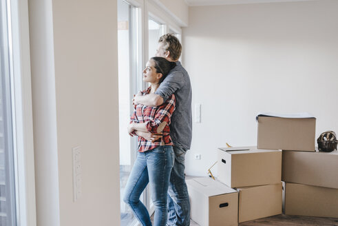 Happy couple standing at window of their new home - JOSF00544