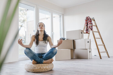 Frau sitzt auf einem Kissen in ihrer neuen Wohnung und meditiert - JOSF00549