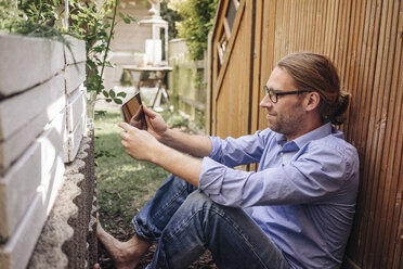 Man relaxing in garden using tablet - JOSF00568