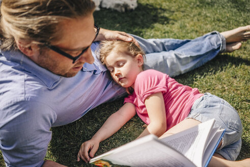 Father reading book to sleeping daughter in garden - JOSF00576